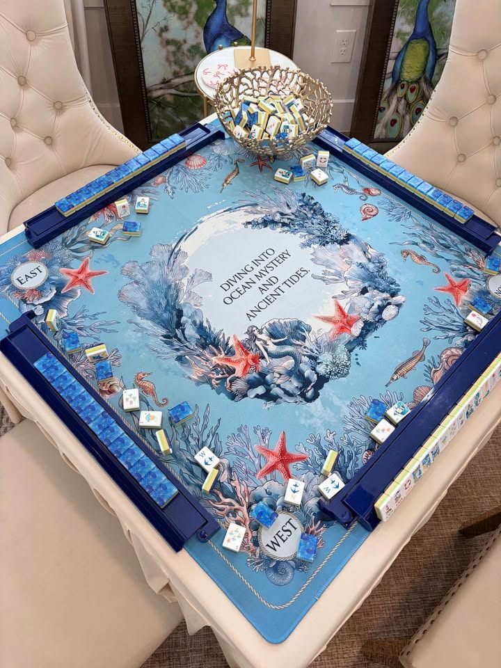 Blue ocean-print mat with starfish, coral, and a mermaid, blue tiles in navy racks on a skirted table