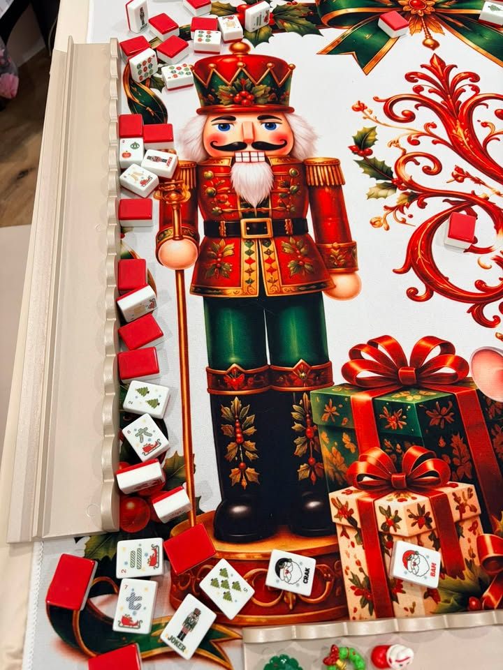 Red-backed mahjong tiles with holiday faces on a mat printed with a nutcracker tin soldier and wrapped gifts